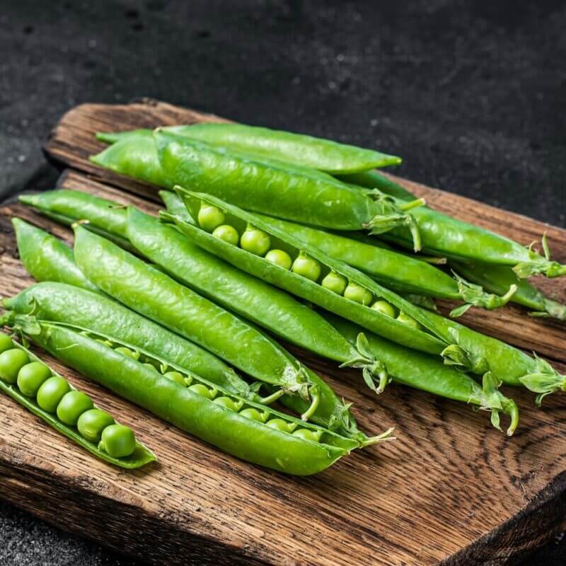 Fresh Peas and green pea pods on a wooden cutting board. Black background. Top view