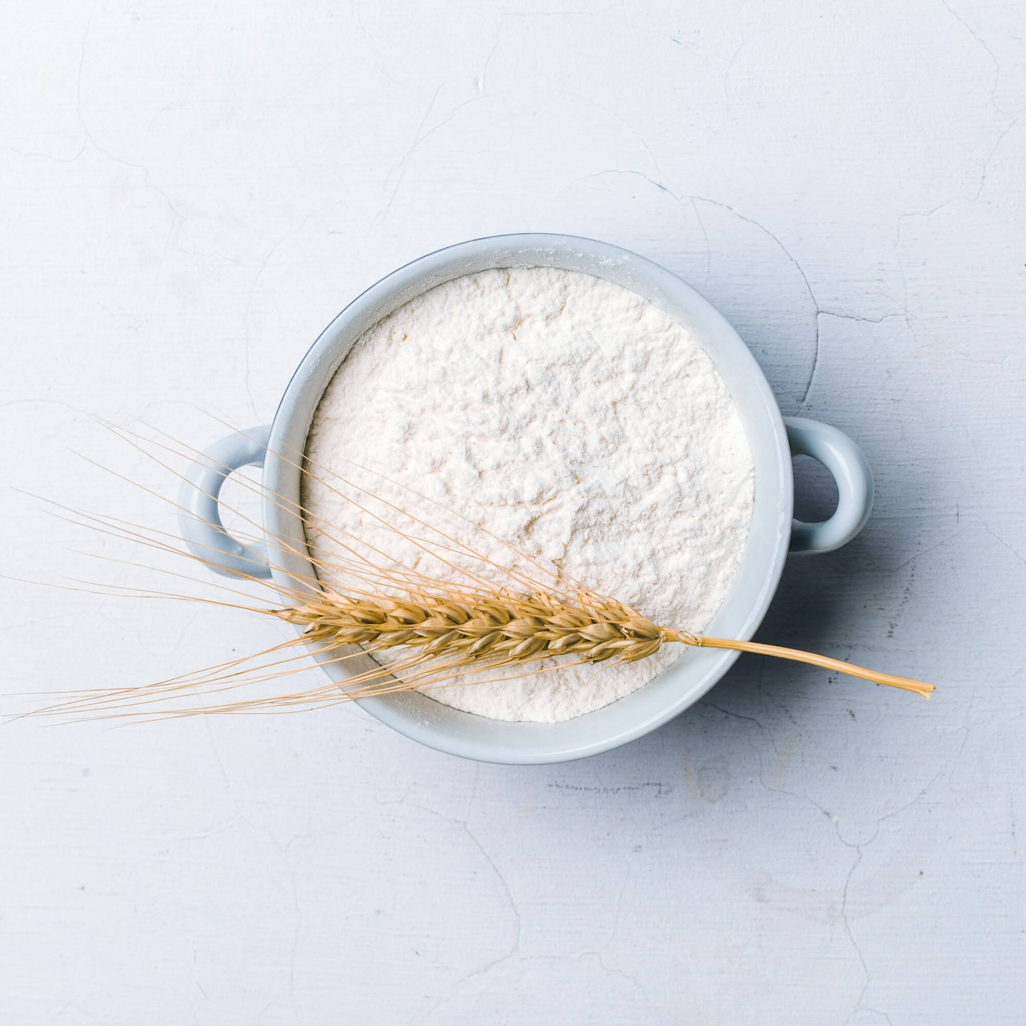 Whole flour in bowl with wheat ears on white background