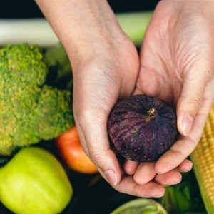 Figs in female hands on a blurred background of vegetables, top view.